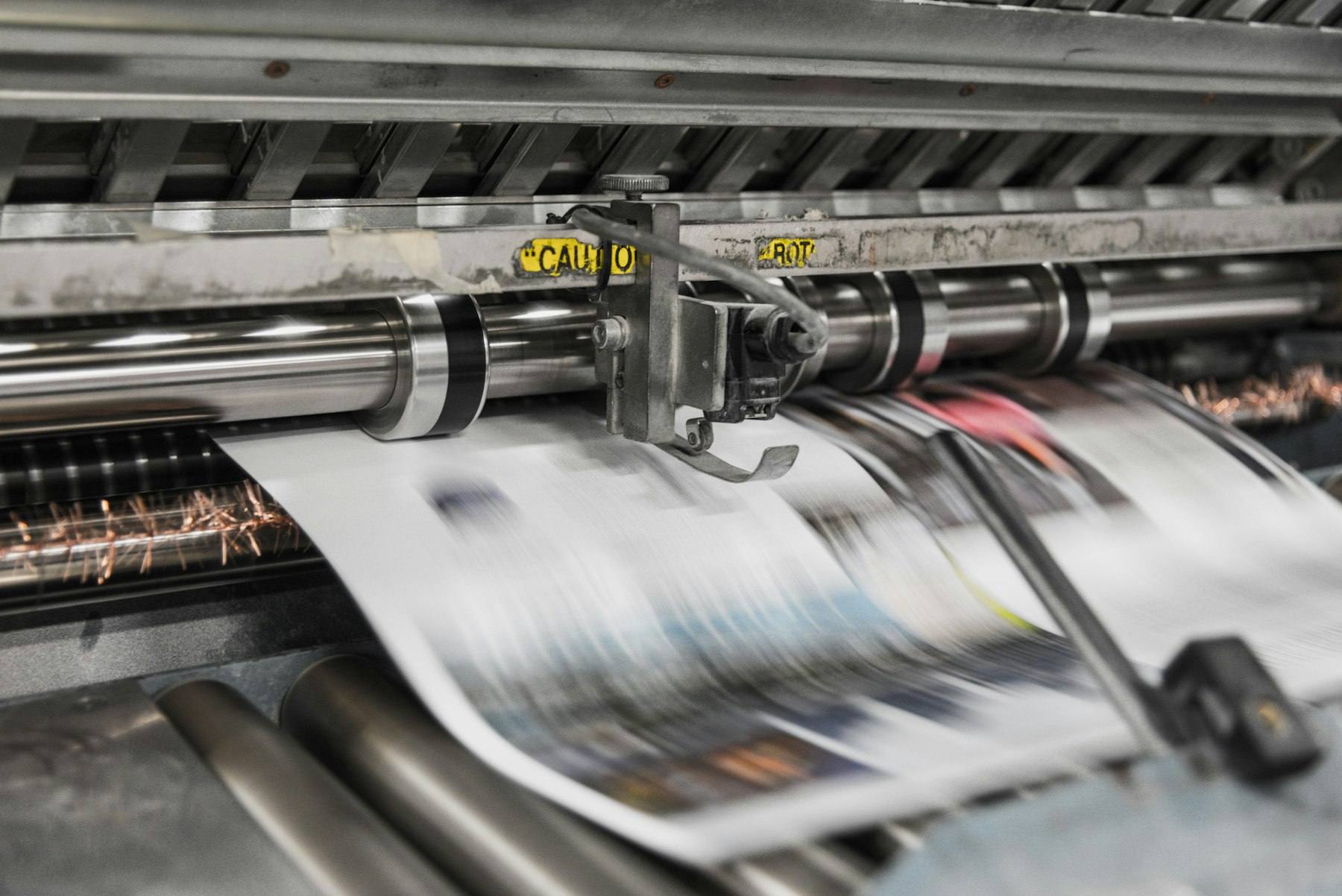 Wide-format press running a printed sheet through the rollers at Dynamic Graphics