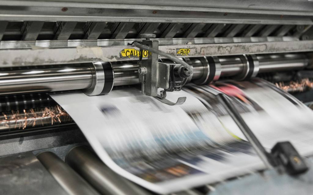 Wide-format press running a printed sheet through the rollers at Dynamic Graphics